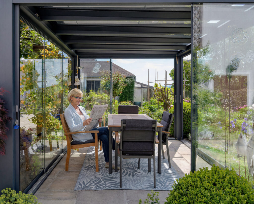 Innenansicht der freistehenden Leeb Atrium Überdachung mit Glasschiebelementen - eine zufriedene Kundin genießt den geschützten Ausblick in den Garten.