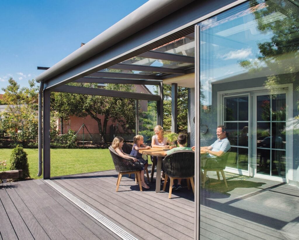 Glückliche Familie genießt das Mittagessen im modernen Leeb Sommergarten mit Glasschiebeelementen - fließender Übergang zum Garten.