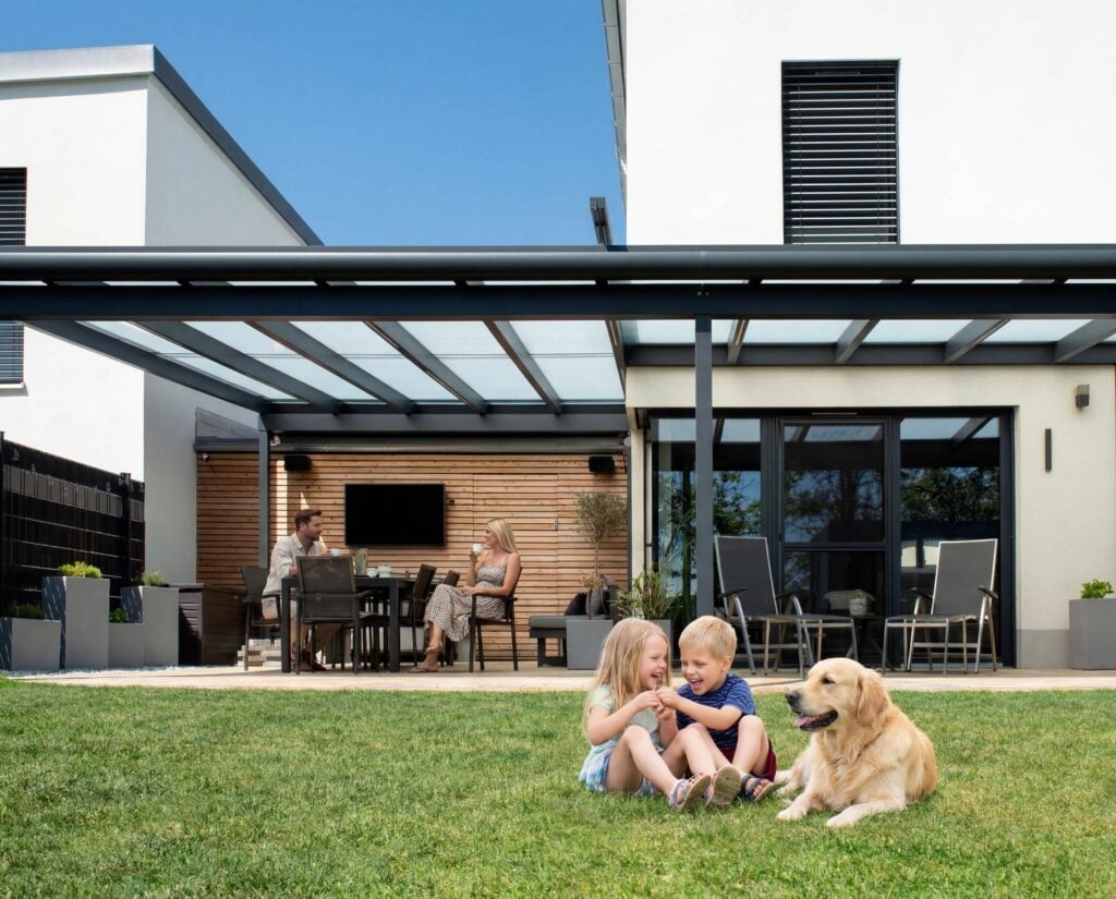 Lebensqualität im Freien: Eine Familie genießt den Nachmittag unter ihrer wetterfesten Leeb Terrassenüberdachung - ein sicherer Rückzugsort für alle Generationen.